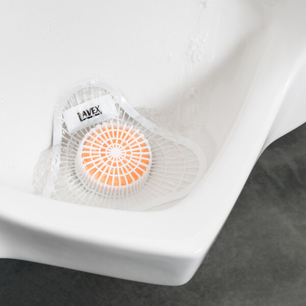 A white urinal with a white circular Lavex urinal screen with orange accents.