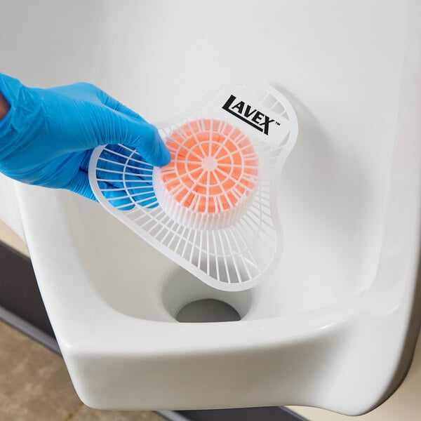 A Lavex urinal screen with a citrus scented block being placed in a urinal.