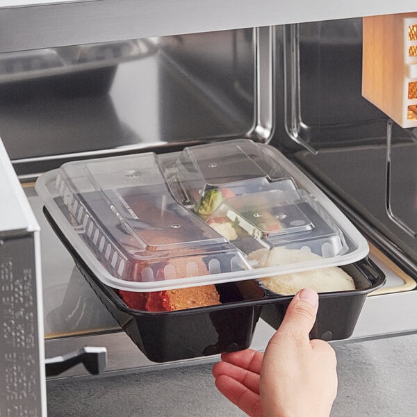 A hand holding a black Choice 3-compartment container with food in it.