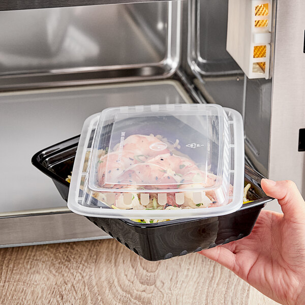 A hand holding a Choice black rectangular plastic microwavable container filled with food.