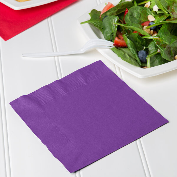 A plate of salad with a purple Creative Converting luncheon napkin.