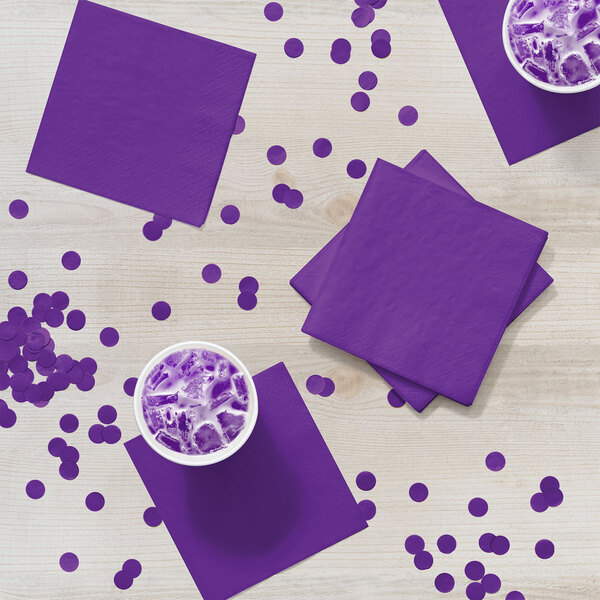 A group of amethyst purple Creative Converting beverage napkins on a table with cups of purple liquid.