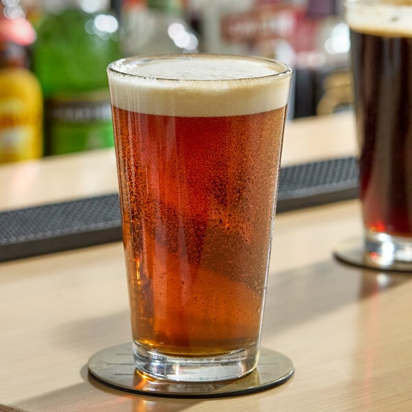 A clear pint glass filled with amber beer and topped with a foamy head, sitting on a coaster.