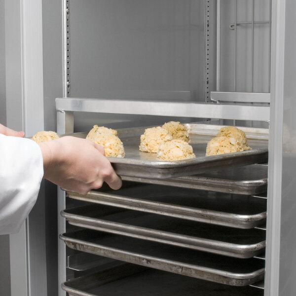 A person holding a Channel sheet pan rack full of food.