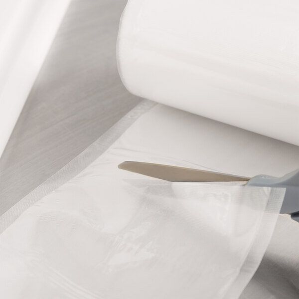 A person using scissors to cut a roll of ARY VacMaster full mesh vacuum packaging bags.