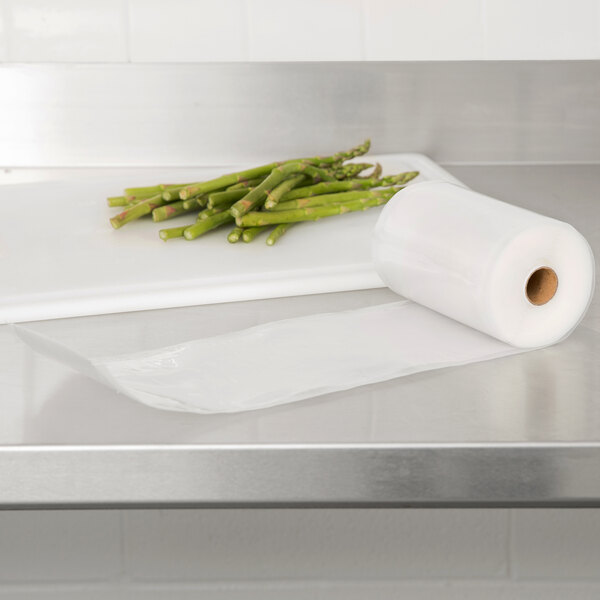 A roll of ARY VacMaster full mesh vacuum packaging bags on a cutting board with asparagus.