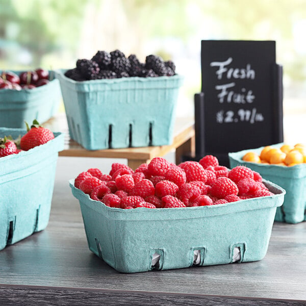 A table with blue and green baskets of fruit, including raspberries, blackberries, and cherries.