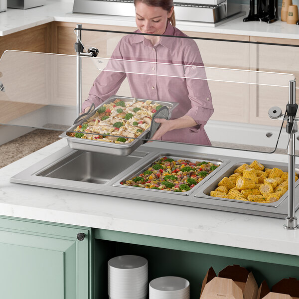 A woman using a Delfield drop-in hot food well to serve food from a counter.