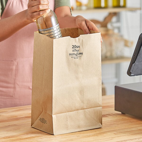 A woman pouring wine from a bottle into a Duro brown paper bag.