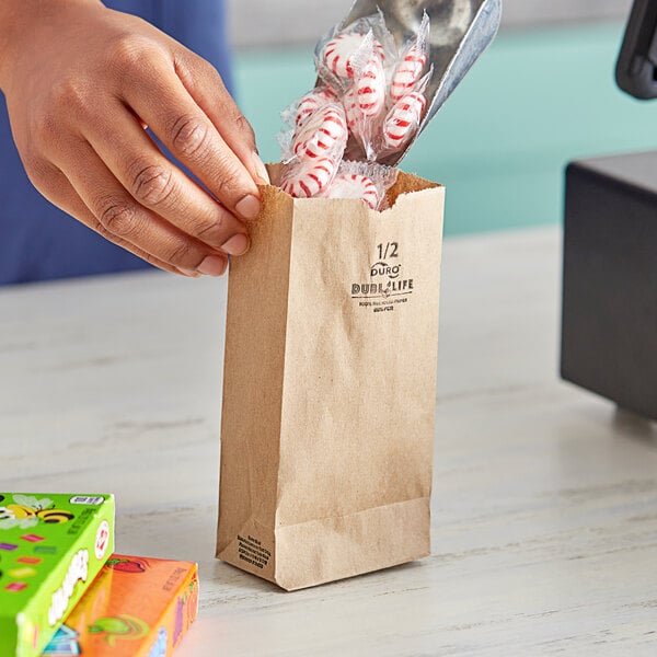 A hand putting candy in a Duro brown paper bag on a convenience store counter.