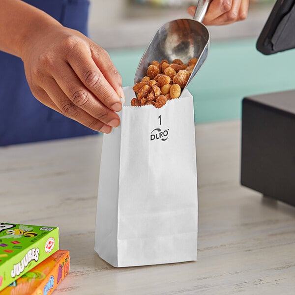 A hand holding a Duro white paper bag with a scoop of peanuts in it.