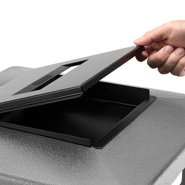 A hand opening a black rectangular container with a black ashtray lid.