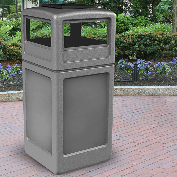 A grey rectangular Commercial Zone waste container with an ashtray dome lid on a brick surface.