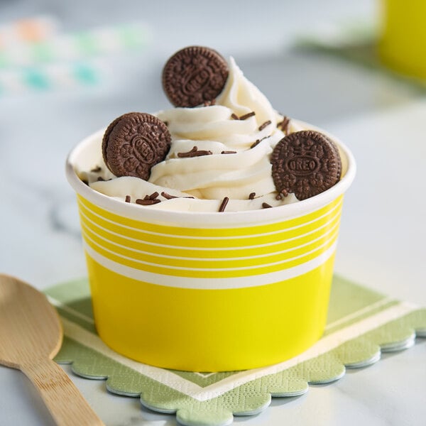 A yellow paper cup filled with frozen yogurt, topped with mini chocolate sandwich cookies and chocolate sprinkles.