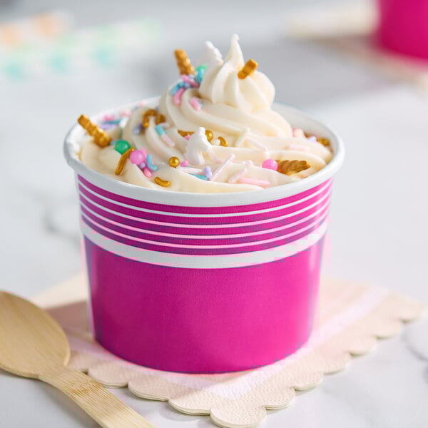 A pink paper frozen yogurt or food cup filled with soft serve and colorful sprinkles.