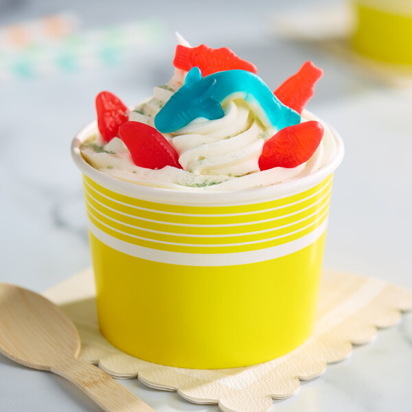 A yellow paper cup filled with frozen yogurt and topped with colorful gummy candies.