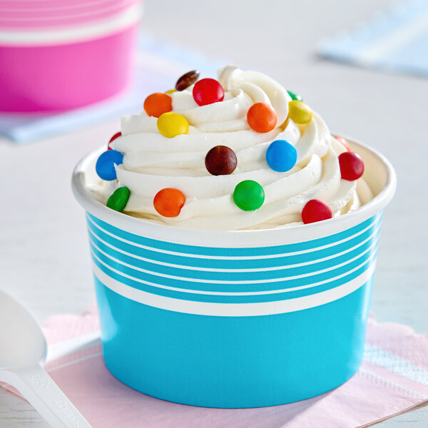 An 8 oz. blue paper frozen yogurt cup filled with swirled vanilla frozen yogurt and topped with colorful candy pieces.