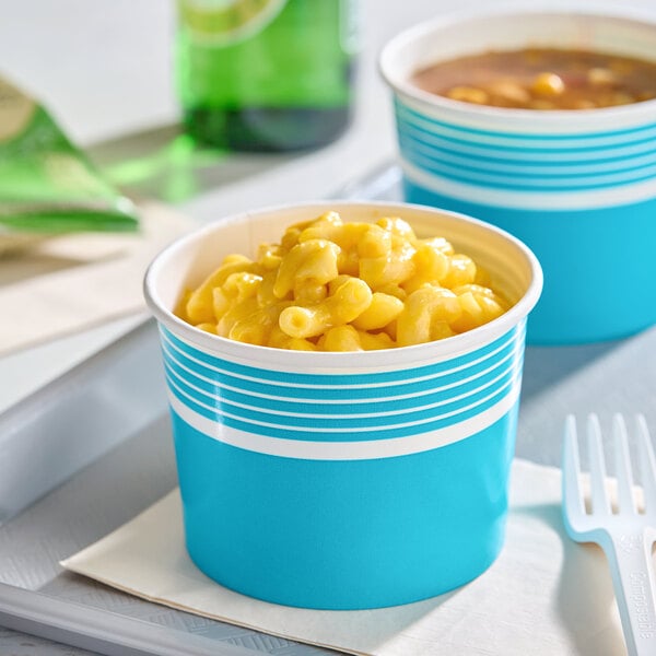 A blue paper food cup filled with macaroni and cheese, placed on a napkin with a plastic fork nearby.