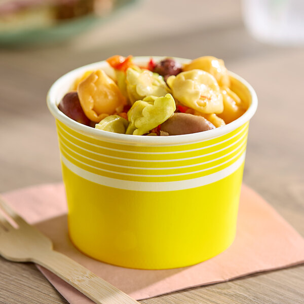 A yellow 12 oz. paper food cup filled with colorful tortellini pasta.