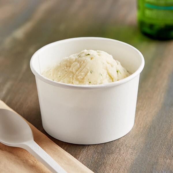 A white paper food cup filled with frozen yogurt with a white plastic spoon on a napkin.