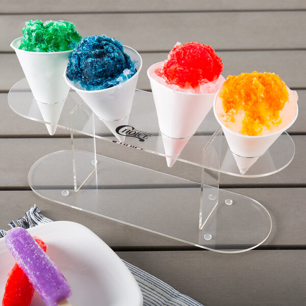 A clear plastic cup of orange and white snow cone syrup with a red and purple popsicle in it.