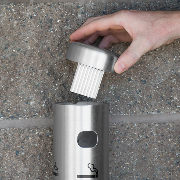 A hand putting a cigarette filter into a Aarco Satin Wall Mounted Cigarette Receptacle.