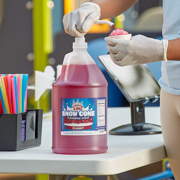 A woman in gloves pouring Carnival King Cherry Snow Cone Syrup into a cup.