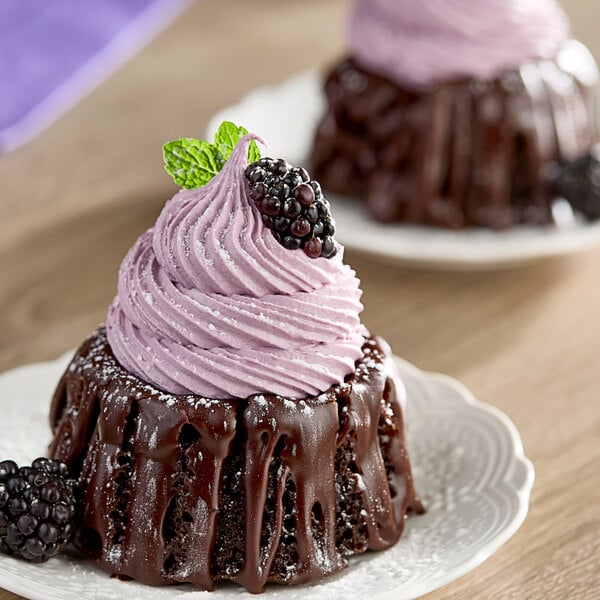 A chocolate cake with purple frosting and blackberries on top next to a bottle of Monin Blackberry Fruit Puree.