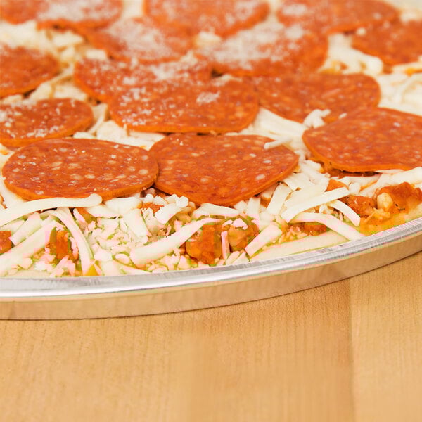 A D&W Fine Pack foil pizza pan with a pizza with pepperoni and cheese on a table.