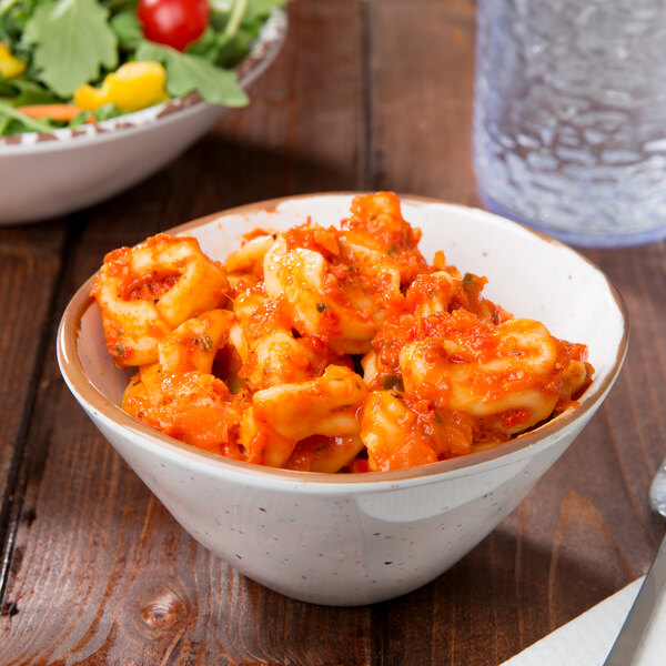 A bowl of pasta with red sauce and a bowl of salad on a table with a glass of water.