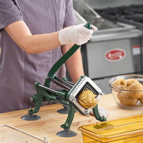 A manual French fry cutter with suction feet being used to slice a potato.