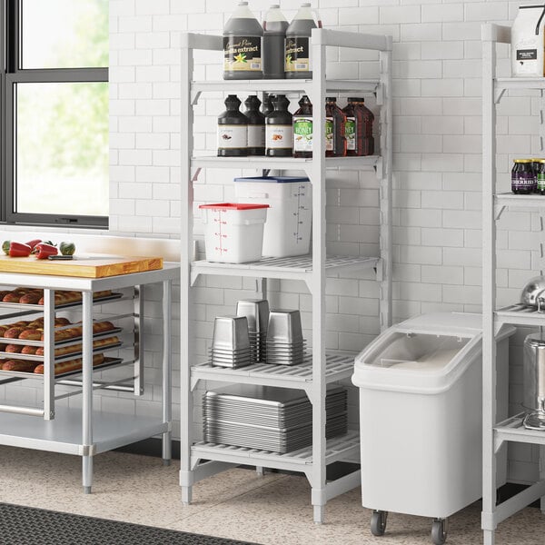 A white Cambro Camshelving® Premium unit with vented shelves holding metal containers.