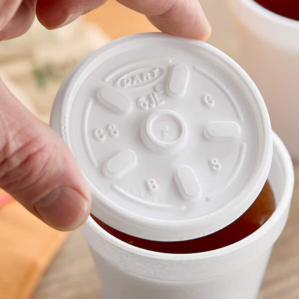 A person holding a Dart white plastic lid on a cup.