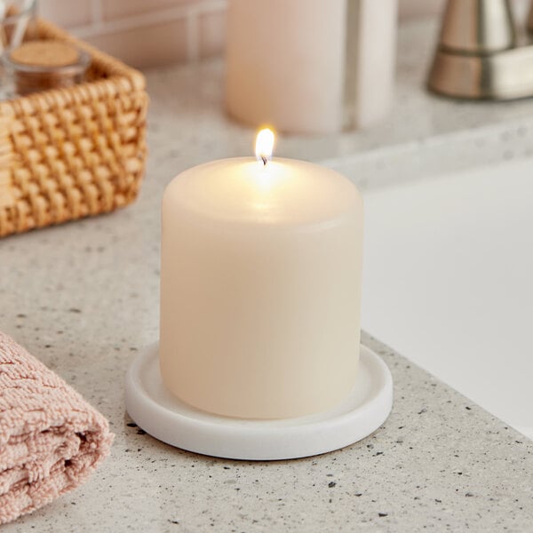 A Hollowick ivory wax pillar candle on a white counter.