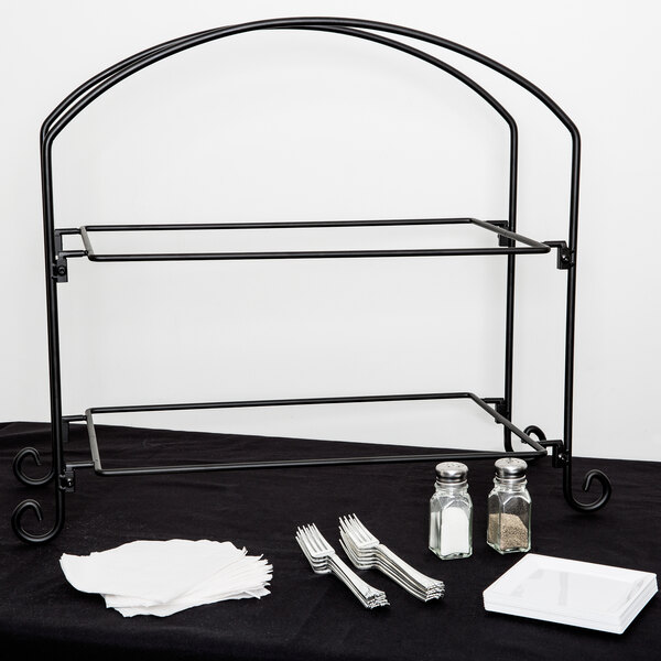 An American Metalcraft black metal two-tier display stand with silverware and napkins on a black table.