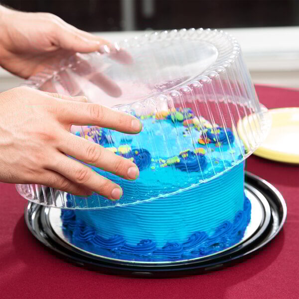 A person using a D&W Fine Pack plastic lid to cover a cake in a plastic container.