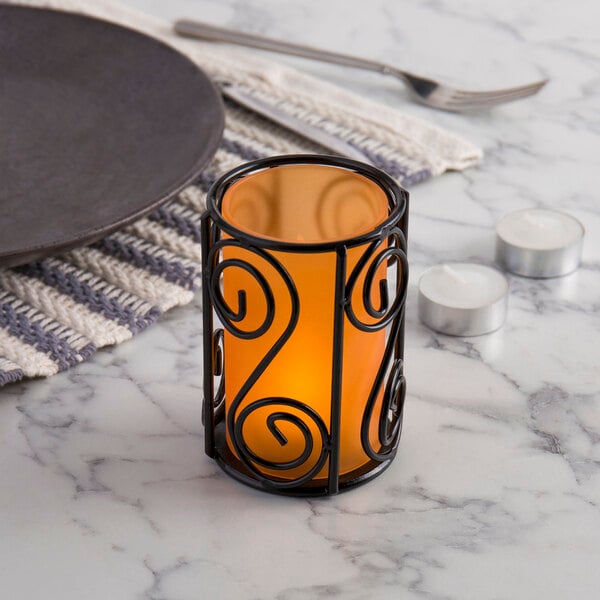 A close-up of a black metal wire candle holder with a candle inside.