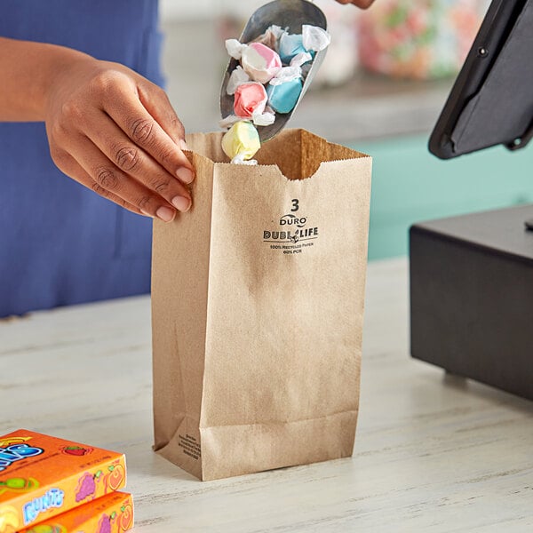 A person holding a Duro brown paper bag full of candy in front of a cash register.