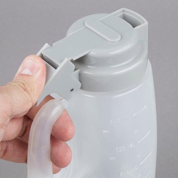 A person holding a Tablecraft 32 oz. plastic dispenser jar with a gray cap.