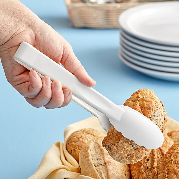 A hand holding a white plastic tong over a pile of bread.