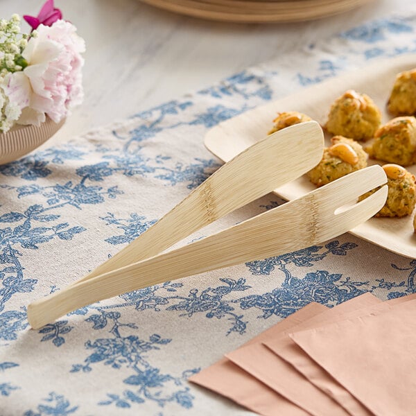 Bambu Veneerware bamboo tongs on a plate with wooden utensils.