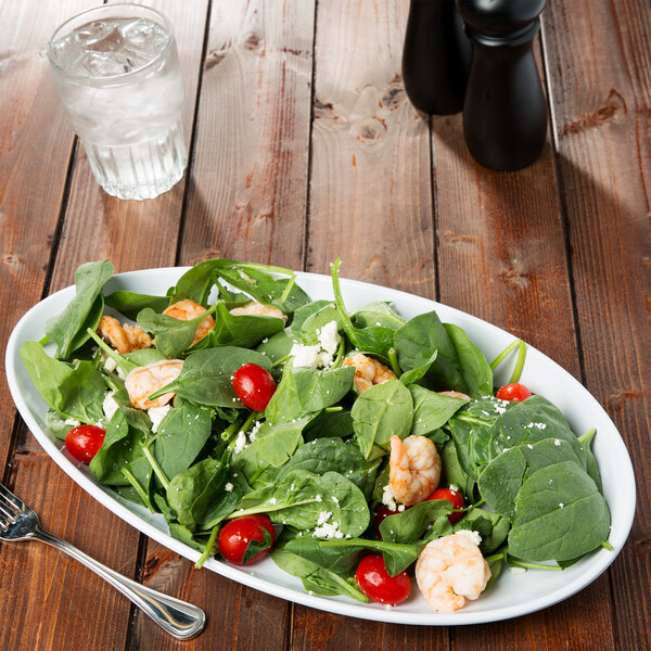 A white oval melamine platter with a salad of shrimp and tomatoes on a table.
