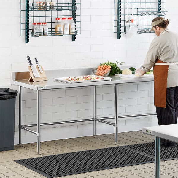 A woman standing at a Regency stainless steel work table in a kitchen preparing carrots.