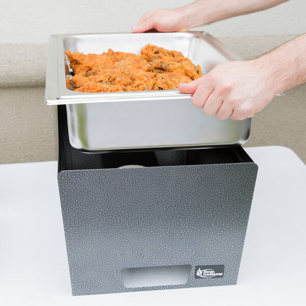 A person holding a tray of food in a Sterno chafer with a lid.