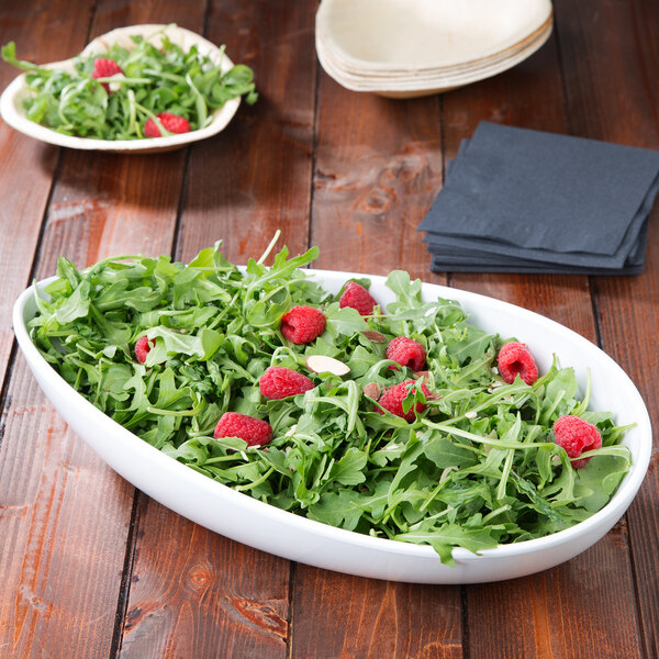 A white oval melamine bowl filled with salad with raspberries.