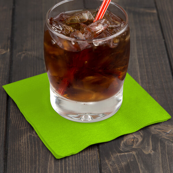 A glass of ice tea with a Fresh Lime Green Creative Converting beverage napkin and a straw.
