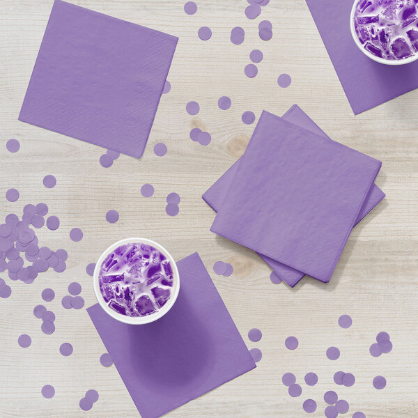 A purple napkin on a table with a cup of purple liquid.