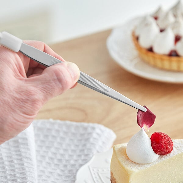 A person holding a rose petal with Mercer Culinary precision tongs over a piece of cake.