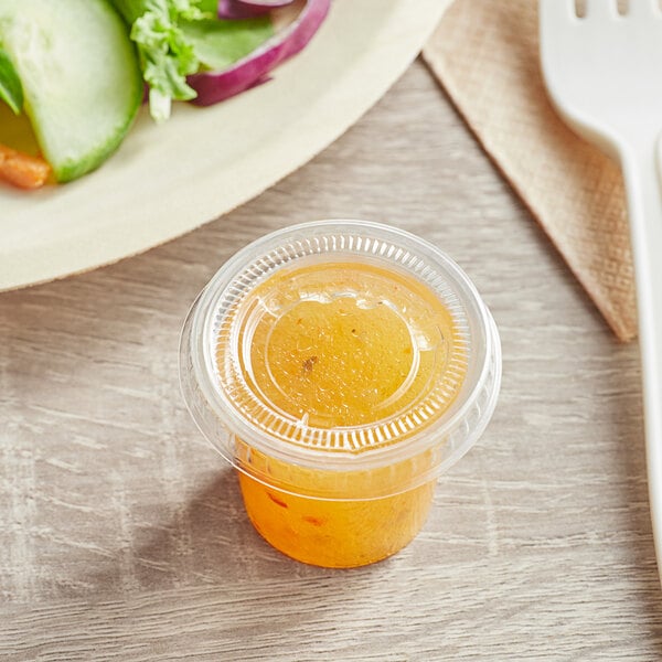 A salad with a Choice plastic souffle cup of yellow liquid on a table.