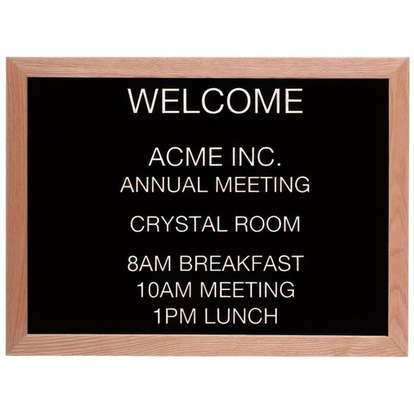 A black Aarco message board with white letters that spell out "Welcome Acme Inc Meeting" on a wooden frame.